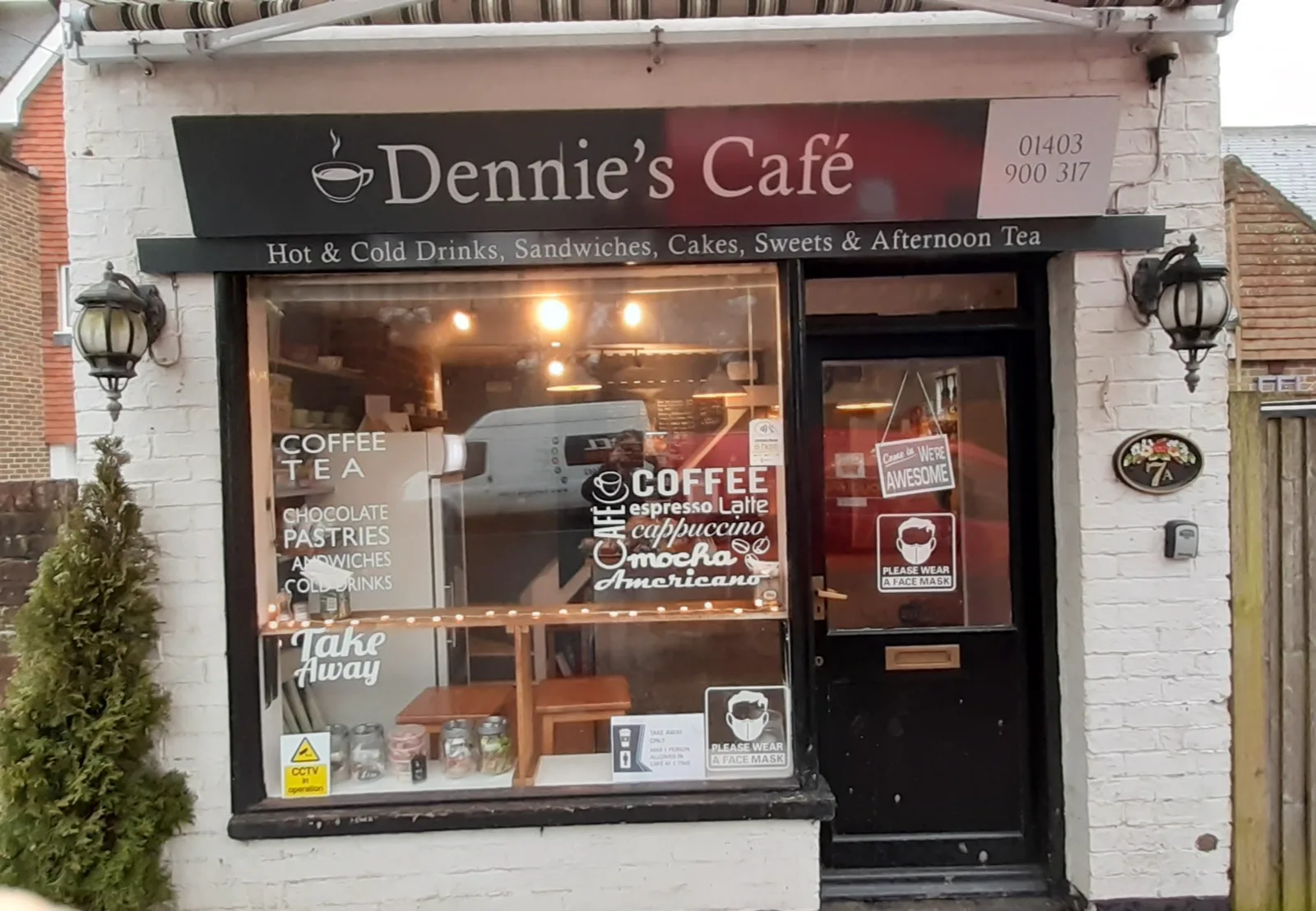 Dennie's Cafe shopfront in Cowfold, with striped awning and hand-lettered menu board